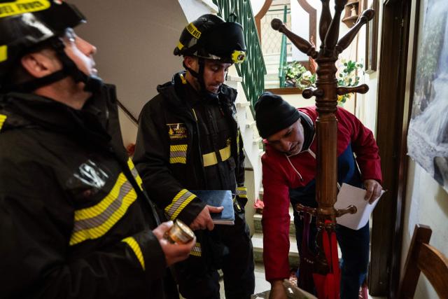 Firefighters help an evacuee in his house in the red zone of the city centre following a landslide that damaged homes in Niscemi on January 28, 2026. More than 1,000 people were evacuated in Sicily after a four-kilometre (2.5-mile) section of cliff crumbled during a storm, leaving houses perched perilously on the edge, authorities said on January 26, 2026. (Photo by MARCO BERTORELLO / AFP)