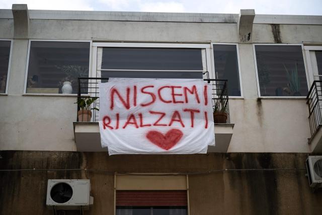 A banner reading "Stand up Niscemi" is hanged on a window in the city centre following a landslide that damaged homes in Niscemi on January 28, 2026. More than 1,000 people were evacuated in Sicily after a four-kilometre (2.5-mile) section of cliff crumbled during a storm, leaving houses perched perilously on the edge, authorities said on January 26, 2026. (Photo by MARCO BERTORELLO / AFP)