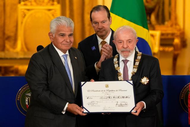 Panama's President Jose Raul Mulino (L) decorates Brazil's President Luiz Inacio Lula da Silva (R) as Panama's Foreign Minister Javier Martinez-Acha applauds at the Palacio de las Garzas in Panama City on January 28, 2026, in the framework of the Latin America and the Caribbean International Economic Forum. The Latin America and Caribbean International Economic Forum 2026, organized by CAF (the Development Bank of Latin America and the Caribbean) in partnership with the Government of Panama, brings together business leaders and regional figures. (Photo by ARNULFO FRANCO / AFP)