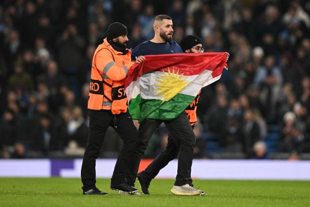 Am pitch invader carries a flag as they are escorted off the pitch during the UEFA Champions League football match between Manchester City and Galatasaray at the Etihad Stadium in Manchester, north west England, on January 28, 2026. (Photo by Oli SCARFF / AFP)