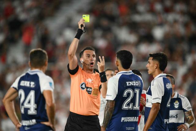 Argentine referee Pablo Dovalo shows a yellow card to Gimnasia y Esgrima La Plata's Uruguayan midfielder #21 Enzo Martinez during the Argentine Professional Football League 2026 Apertura Tournament match between River Plate and Gimnasia y Esgrima La Plata at the Mas Monumental Stadium in Buenos Aires on January 28, 2026. (Photo by Luis ROBAYO / AFP)