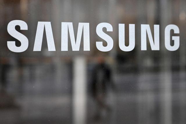 A man walks past the logo of Samsung Electronics displayed on a glass door at the company's Seocho building in Seoul on January 29, 2026. South Korean tech giant Samsung Electronics posted record quarterly profits on January 29, riding strong market demand for its artificial intelligence chips. (Photo by Jung Yeon-je / AFP)