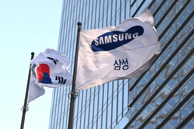 A South Korean national flag (L) and a Samsung flag flutter outside the company's Seocho building in Seoul on January 29, 2026. South Korean tech giant Samsung Electronics posted record quarterly profits on January 29, riding strong market demand for its artificial intelligence chips. (Photo by Jung Yeon-je / AFP)