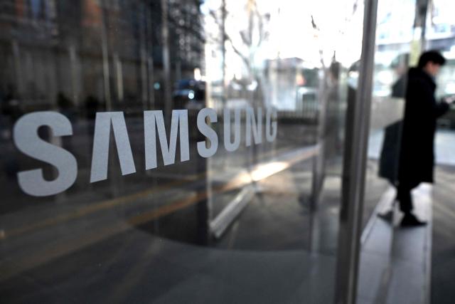 A man walks past the logo of Samsung Electronics displayed on a glass door at the company's Seocho building in Seoul on January 29, 2026. South Korean tech giant Samsung Electronics posted record quarterly profits on January 29, riding strong market demand for its artificial intelligence chips. (Photo by Jung Yeon-je / AFP)