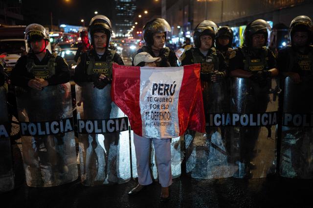 A demonstrator shows a peruvian flag in front of riot police officers during a protest march called by Generation Z demanding the resignation of President Jeri in Lima on January 28, 2026. Peru's interim president, Jose Jeri, said on January 21 that he is the victim of a plot to force his resignation, in an appearance before a congressional committee investigating him for alleged influence peddling over a secret meeting with a Chinese businessman. (Photo by Ernesto BENAVIDES / AFP)