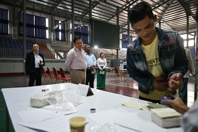 (FILES) Myanmar's military chief Min Aung Hlaing (front C) looks on during his visit to a polling station as a voter (R) gets his finger inked during the third and final phase of Myanmar's general election in Mandalay on January 25, 2026. The colour of the winning party in Myanmar's junta-run election is the same green as a general's uniform, its staff are retired senior officers, and most expect it to march in lockstep with the military. The Union Solidarity and Development Party (USDP) claimed an overwhelming victory that indicates the country's armed forces, known as the Tatmadaw, intend to preserve their grip on power. But the top brass' decision to cloak its command in civilian dress means ceding some of junta chief Min Aung Hlaing's singular authority, analysts say. (Photo by ANTHONY WALLACE / AFP)