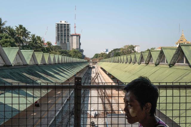 A man crosses an elevated walkway above train platforms at Yangon Central Station in Yangon on January 28, 2026. Yangon’s Circular Railway is a 45.9 km commuter rail loop with 39 stations that connects the city center to its suburbs. Built by the British in the 1930’s, it remains one of the cheapest and most used transport options for local commuters, with a complete circuit taking about three hours to travel. (Photo by ANTHONY WALLACE / AFP)