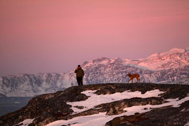 A man walks with his dog at the coastline of the city in Nuuk, western Greenland, with a slightly snow covered mountain in the background,  on January 28, 2026. (Photo by Ina FASSBENDER / AFP)