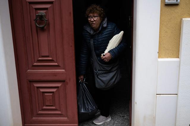 A woman leaves her house with a statue of the Virgin Mary as she returns with firefighters to collect her belongings in the red zone of Niscemi, Sicily, on January 29, 2026. A large area of the town of Niscemi is declared  "red zone" after the a 4km-long stretch of the hillside collapsed on January 25, 2026, forcing the evacuation of some 1,500 people. The town, built on unstable terrain, was battered by a powerful storm which hit southern Italy last week and experts say the chasm could widen further and swallow houses with the rains expected over the coming days. (Photo by MARCO BERTORELLO / AFP)