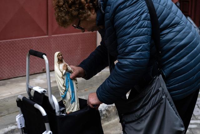 A woman leaves her house with a statue of the Virgin Mary as she returns with firefighters to collect her belongings in the red zone of Niscemi, Sicily, on January 29, 2026. A large area of the town of Niscemi is declared  "red zone" after the a 4km-long stretch of the hillside collapsed on January 25, 2026, forcing the evacuation of some 1,500 people. The town, built on unstable terrain, was battered by a powerful storm which hit southern Italy last week and experts say the chasm could widen further and swallow houses with the rains expected over the coming days. (Photo by MARCO BERTORELLO / AFP)