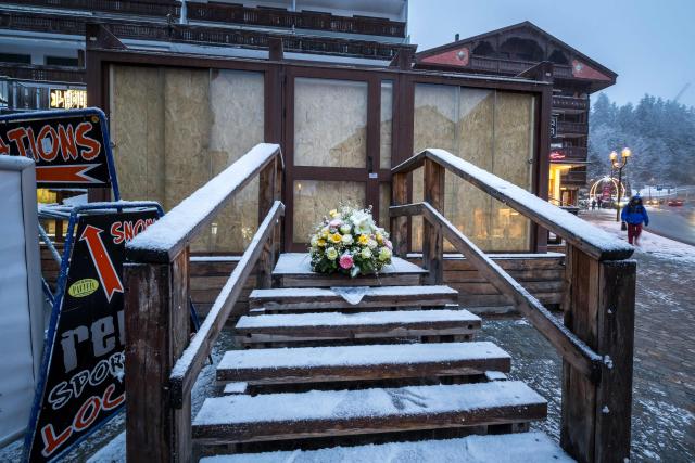 This photograph shows a bouquet of flowers left by members of the Italy's alpine ski team, which takes part in the World Cup races in Crans-Montana, at the entrance of the bar Le Constellation in tribute to the victims of the fire that ripped through the venue on New Year's Eve celebrations, in the Alpine ski resort town of Crans-Montana on January 28, 2026. The fire on January 1 at the bar Le Constellation left 40 people dead -- including nine French and six Italian nationals -- and injured 116 others, most of them teenagers. (Photo by Fabrice COFFRINI / AFP)