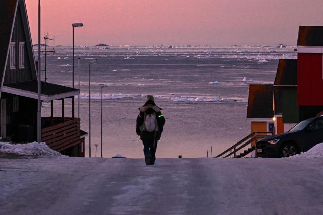 A woman walks in a snow-covered street as the sea seen in background is covered with sheets of ice in Nuuk, Greenland, on January 29, 2026. (Photo by Ina FASSBENDER / AFP)