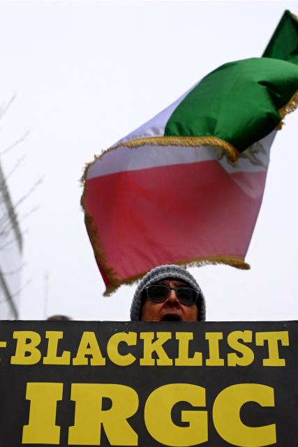 A supporter of the National Council of Resistance of Iran waves a pre-1979 Islamic Revolution Iranian flag and holds a placard reading "Blacklist Islmamic Revolutionary Guard Corps" as he takes part in a demonstration in support of the Iranian people in Brussels on January 29, 2026. (Photo by Nicolas TUCAT / AFP)