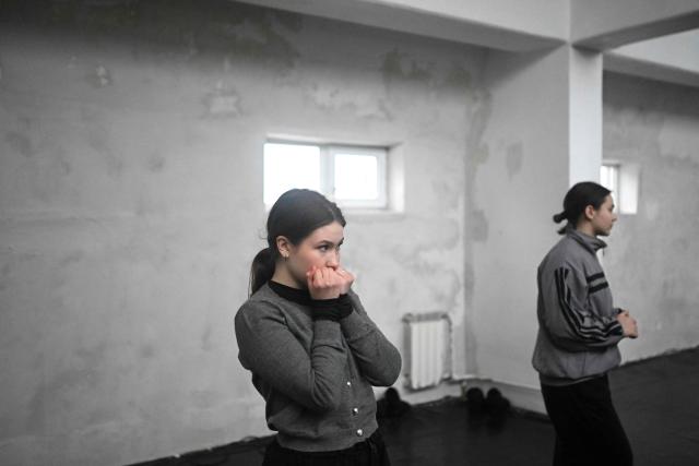 A dancer warms her hands as she listens to explanations by a choreographer of the dance team "Baza art people" during a rehearsal of the contemporary ballet "Paper Tigers" at an unheated dance studio in Kyiv on January 29, 2026, amid the Russian invasion of Ukraine. (Photo by Sergei GAPON / AFP)