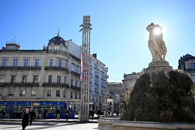 Pedestrians walk past a tramway and the Fontaine des Trois Grвces at Place de la Comedie in Montpellier, southern France, on January 29, 2026. Free transportation is a popular idea for the March municipal elections in many cities. But the promises vary greatly, and some candidates denounce it as “vote fishing” or even a “false good idea.” Initially limited to young people and seniors, then to weekends, this promise made in 2020 for Montpellier has, for a little over two years now, been available on buses and trams to all 500,000 residents of this metropolitan area. (Photo by Gabriel BOUYS / AFP)