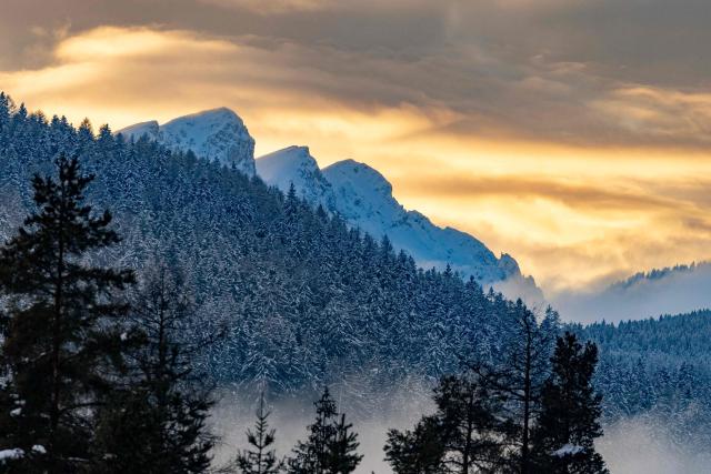 The setting sun cutting through the clouds colours the sky yellow behind the mountain peaks outside the village of Niederdorf (Villabassa), between the Olympic venues in Cortina and Antholz, northern Italy prior to the Milano Cortina 2026 Olympic Games, on January 29, 2026. (Photo by Odd ANDERSEN / AFP)