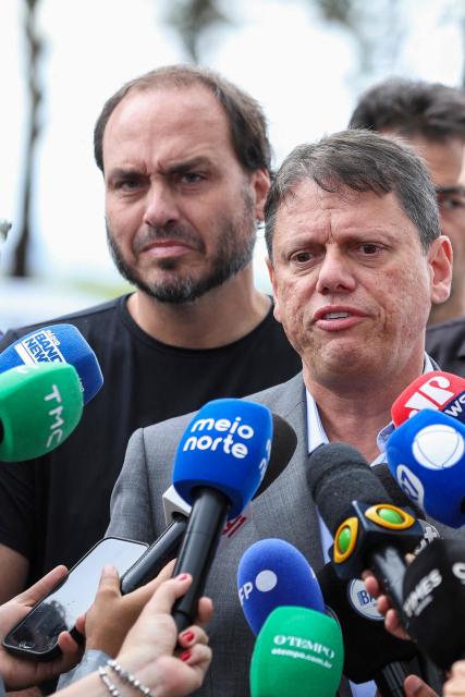 Tarcisio de Freitas (C), governor of the state of Sao Paulo, speaks to reporters accompanied by Carlos Bolsonaro, son of former Brazilian President Jair Bolsonaro, after visiting Jair Bolsonaro, imprisoned at the Papuda penitentiary complex in Brasilia, on January 29, 2026. (Photo by Sergio Lima / AFP)
