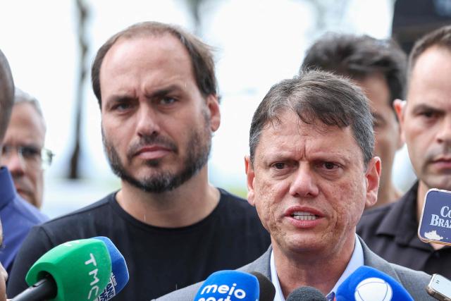 Tarcisio de Freitas (C), governor of the state of Sao Paulo, speaks to reporters accompanied by Carlos Bolsonaro, son of former Brazilian President Jair Bolsonaro, after visiting Jair Bolsonaro, imprisoned at the Papuda penitentiary complex in Brasilia, on January 29, 2026. (Photo by Sergio Lima / AFP)