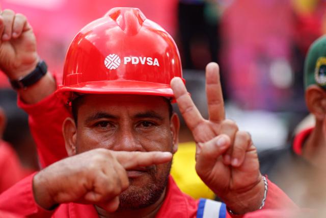 A worker of Venezuelan state oil company PDVSA makes hand signs during a march called by the United Socialist Party of Venezuela (PSUV) in support of the Hydrocarbons Law and demanding the release of ousted President Nicolas Maduro, in Caracas on January 29, 2026. (Photo by Pedro MATTEY / AFP)