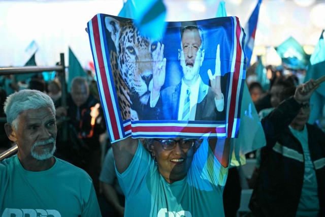 A supporter of Costa Rica’s Sovereign People party presidential candidate Laura Fernandez holds a flag bearing an image of Costa Rican President Rodrigo Chaves Robles during a Fernandez campaign closing event in San Jose on January 29, 2026. Costa Rica will hold a presidential election on February 1, 2026. (Photo by Marvin RECINOS / AFP)