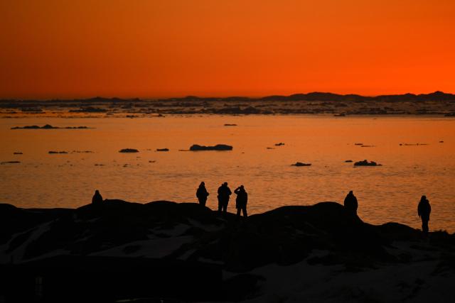 People stand at the coastline of Nuuk, Greenland, as sun sets on January 29, 2026. (Photo by Ina FASSBENDER / AFP)
