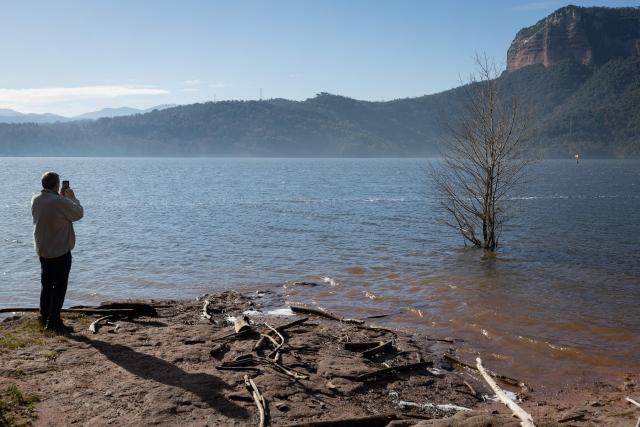 A person takes pictures on the shore of the reservoir of Sau in Vilanova de Sau in Catalonia amid high water-level, on January 30, 2026. This long-Term project shows photos of the same places taken every month over a very long period. (Photo by Josep LAGO / AFP)