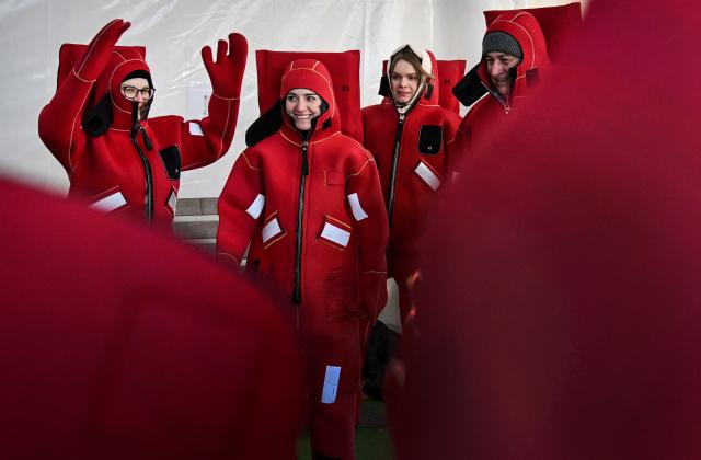 Participants wearing isothermal wetsuits warm up as they get ready to float among ice floes in a hole on the frozen Moskva river during an ice floating session - the growing relaxation trend, in Moscow on January 30, 2026. (Photo by Alexander NEMENOV / AFP)