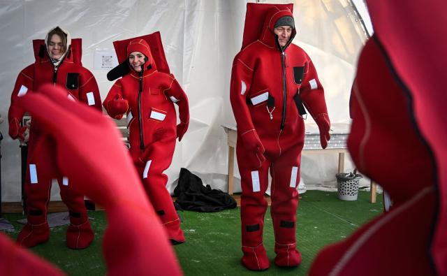 Participants wearing isothermal wetsuits warm up as they get ready to float among ice floes in a hole on the frozen Moskva river during an ice floating session - the growing relaxation trend, in Moscow on January 30, 2026. (Photo by Alexander NEMENOV / AFP)
