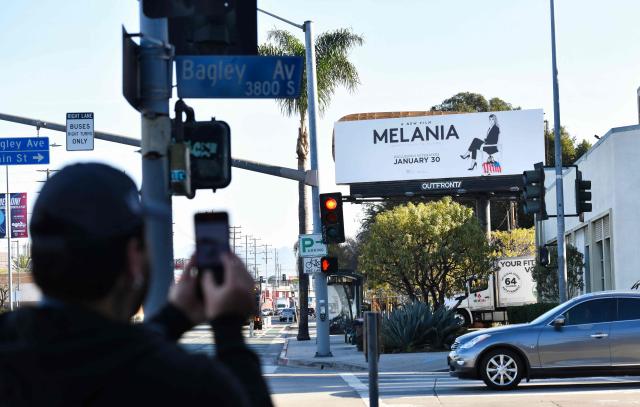 A man takes a picture of a billboard advertising the film "Melania" defaced with graffiti attributed to the activist art collective INDECLINE in Culver City, California on January 30, 2026. (Photo by Chris Delmas / AFP)