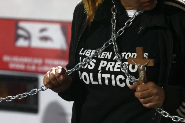 A person holds a crucifix and chains to demand the release of political prisoners outside the Zone 7 prison of the Bolivarian National Police (PNB) in Caracas on January 30, 2026. (Photo by Pedro MATTEY / AFP)