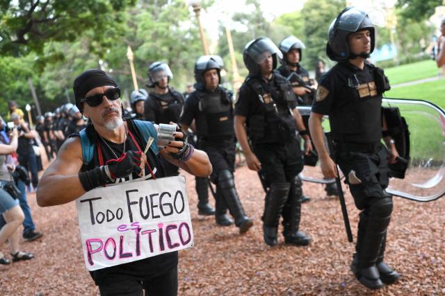 A man shows a sign that reads "All fire is political" past riot police officers during a protest to demand more help to combat wildfires in Patagonia from Argentina's President Javier Milei government in Buenos Aires on January 30, 2026. Argentina's government on declared an emergency in Patagonia on January 29, 2026, where wildfires have ripped through vast tracts of forest since the start of the Southern Hemisphere summer. (Photo by Luis ROBAYO / AFP)