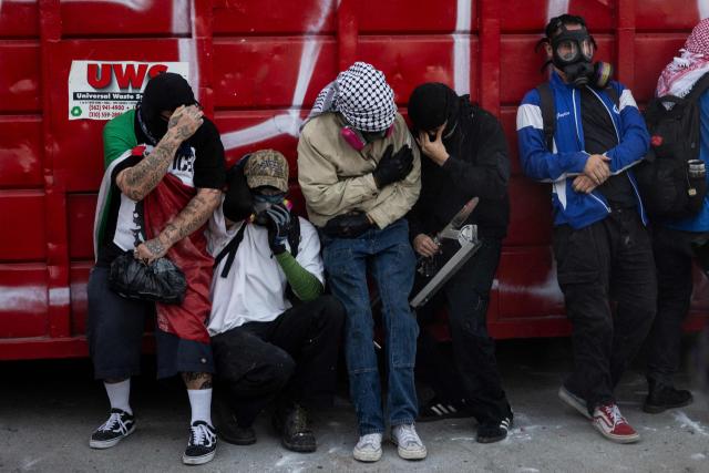 Protesters take shelter behind a dumpster that they moved in an attempt to barricade police during a "National Shutdown" protest against US Immigration and Customs Enforcement in Los Angeles on January 30, 2026. Donald Trump's border chief said January 29, 2026 that some federal agents could be withdrawn from Minneapolis, the northern US city that has become the flashpoint for the president's immigration crackdown. The Trump administration, facing a public backlash over the shooting deaths of two Americans by federal agents in Minneapolis, also eased immigration operations in the northeastern state of Maine. (Photo by ETIENNE LAURENT / AFP)