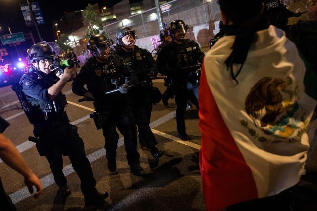 An LAPD officer aims his non-lethal ammunition weapon to a protester draped in a Mexican flag during a "National Shutdown" protest against US Immigration and Customs Enforcement in Los Angeles on January 30, 2026. Donald Trump's border chief said January 29, 2026 that some federal agents could be withdrawn from Minneapolis, the northern US city that has become the flashpoint for the president's immigration crackdown. The Trump administration, facing a public backlash over the shooting deaths of two Americans by federal agents in Minneapolis, also eased immigration operations in the northeastern state of Maine. (Photo by ETIENNE LAURENT / AFP)