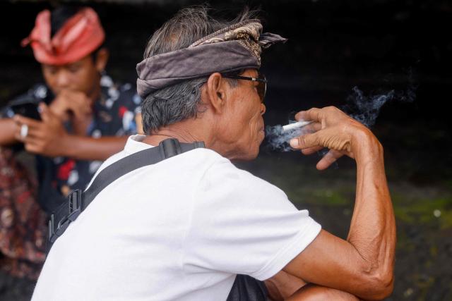 Hindu men wearing the traditional Balinese "udeng" headband smoke at Tanah Lot temple in Tabanan, Indonesia's Bali island, on January 31, 2026. (Photo by David GANNON / AFP)