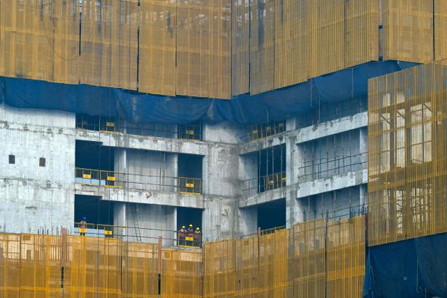 Workers look out from the site of an under construction building in Mumbai on January 31, 2026. (Photo by Indranil Mukherjee / AFP)
