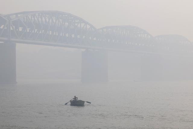 A man rows a boat in the river Ganges near the Raj Ghat bridge amid smoggy conditions in Varanasi on January 31, 2026. (Photo by Niharika KULKARNI / AFP)