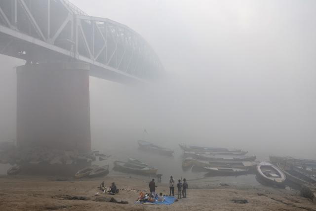 People stand along the banks of river Ganges amid smoggy conditions in Varanasi on January 31, 2026. (Photo by Niharika KULKARNI / AFP)