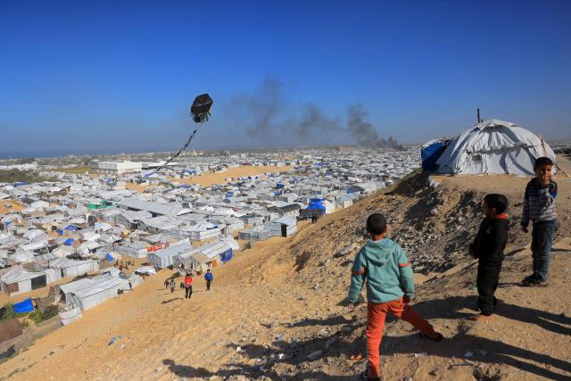 Boys fly a kite against the backdrop of smoke rising from the Gath shelter, that houses displaced Palestinians, after an Israeli air strike in the west of Khan Yunis, southern Gaza Strip on January 31, 2026. Israeli air strikes killed 11 people in the Gaza Strip on January 31, according to the territory's ministry of health, including people sheltering in a tent in the south. (Photo by Bashar Taleb / AFP)