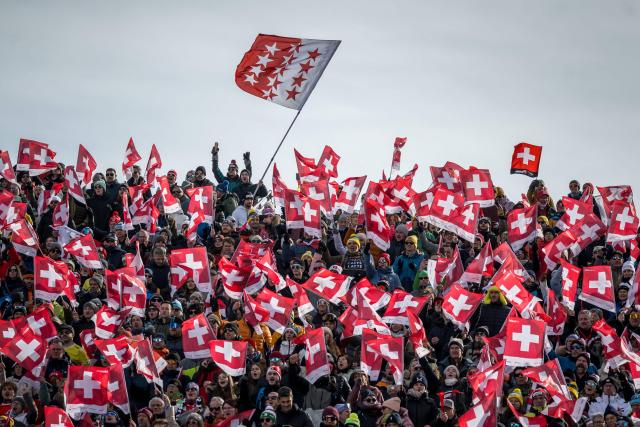 Supporters wave Swiss national flags and a Canton of Valais flag (up C) as they cheer during the women's super G race part of the FIS Alpine Ski World Cup 2025-2026, in Crans Montana, Switzerland, on January 31, 2026. (Photo by Fabrice COFFRINI / AFP)