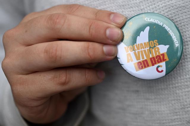 A supporter of Costa Rican presidential candidate Claudia Dobles shows a pin button reading "Let's live in peace again" during a gathering with her in San Jose on January 31, 2026, the day before the presidential election. (Photo by MARVIN RECINOS / AFP)