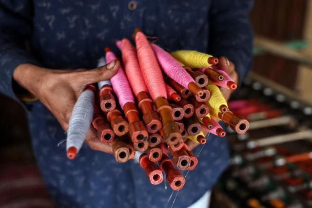 A worker carries threads to weave sarees and dress material on power looms at a workshop in Varanasi on February 1, 2026. (Photo by Niharika KULKARNI / AFP)