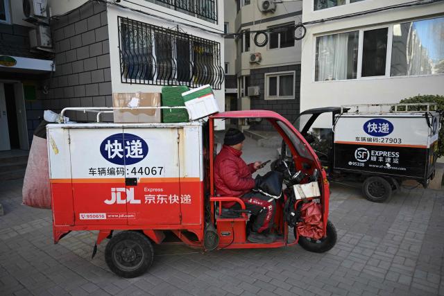 A worker drives a vehicle for the delivery of online purchased products in a residential area in Beijing on February 1, 2026. (Photo by Pedro PARDO / AFP)