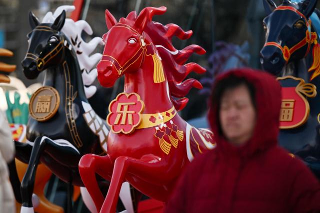 A woman walks past a decoration ahead of the Lunar New Year of the Horse in Beijing on February 1, 2026. (Photo by Pedro PARDO / AFP)