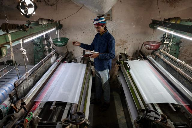 A worker weaves sarees and dress material on power looms at a workshop in Varanasi on February 1, 2026. (Photo by Niharika KULKARNI / AFP)