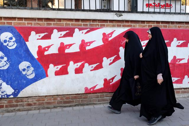 Women walk past a mural painted on the outer walls of the former US embassy in Tehran, colloquially-referred to as the "Spy Den,"on February 1, 2026. Iran's supreme leader Ayatollah Ali Khamenei warned on February 1 of a "regional war" if the United States attacked following heavy military deployments by Washington in the Gulf. (Photo by ATTA KENARE / AFP)