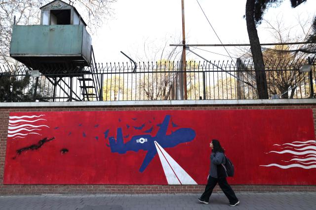 A woman walks past a mural depicting a US drone painted on the outer walls of the former US embassy in Tehran, colloquially-referred to as the "Spy Den,"on February 1, 2026. Iran's supreme leader Ayatollah Ali Khamenei warned on February 1 of a "regional war" if the United States attacked following heavy military deployments by Washington in the Gulf. (Photo by ATTA KENARE / AFP)
