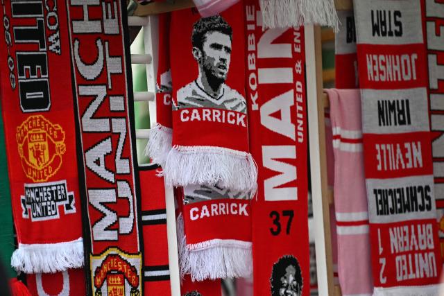 Scarves, including one of Manchester United's English Interim head coach Michael Carrick, are seen for sale on a merchandise stall outside the ground ahead of the English Premier League football match between Manchester United and Fulham at Old Trafford in Manchester, north west England, on February 1, 2026. (Photo by Paul ELLIS / AFP)