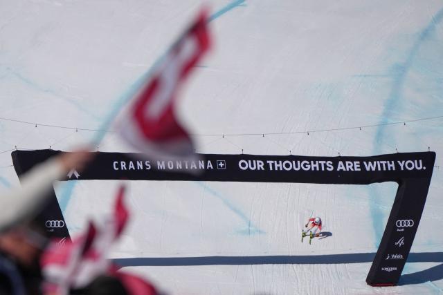 Switzerland's Gael Zulauf crosses the finish line as supporters wave Swiss national flags during the men's downhill race part of the FIS Alpine Ski World Cup 2025-2026, in Crans Montana, Switzerland, on February 1, 2026. (Photo by Maxime Schmid / AFP)