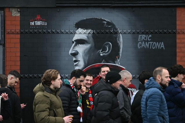 Arriving Manchester United fans pass a picture of club legend Eric Cantona outside the ground ahead of the English Premier League football match between Manchester United and Fulham at Old Trafford in Manchester, north west England, on February 1, 2026. (Photo by Paul ELLIS / AFP)