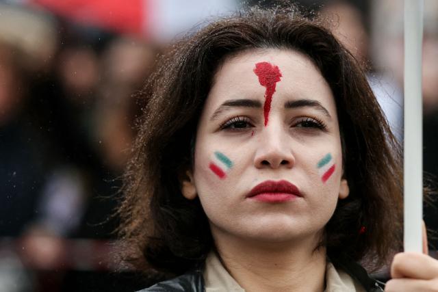 A protester with her face painted in red and with the colour of the Iranian flag, takes part in a March for Iran in support of the Iranian people, called by pro-royalists and supporters of the son of the last shah of Iran Mohammad Reza Pahlavi, on Place Vauban, in Paris on February 1, 2026. (Photo by Alain JOCARD / AFP)